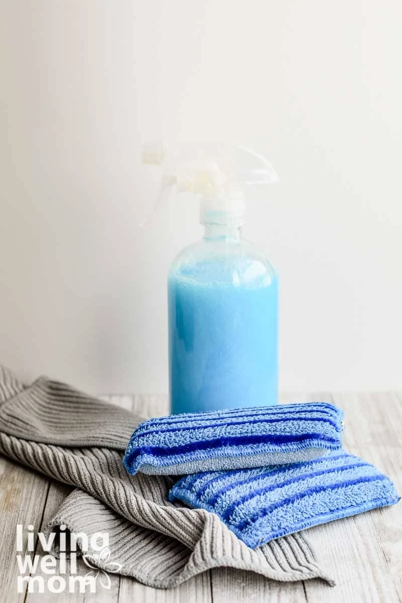 homemade shower cleaner in glass bottle with sponges and cleaning cloths